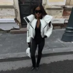 Stylish woman in black outfit with white puffer jacket and sunglasses on city street.